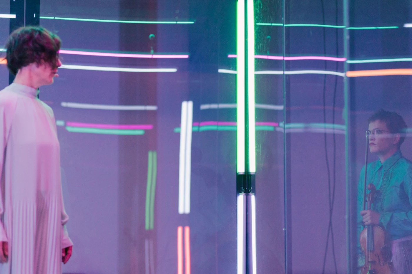 Eine Frau schaut in einem verspiegelten Raum durch Scheiben auf eine andere Person hinter dem Glas