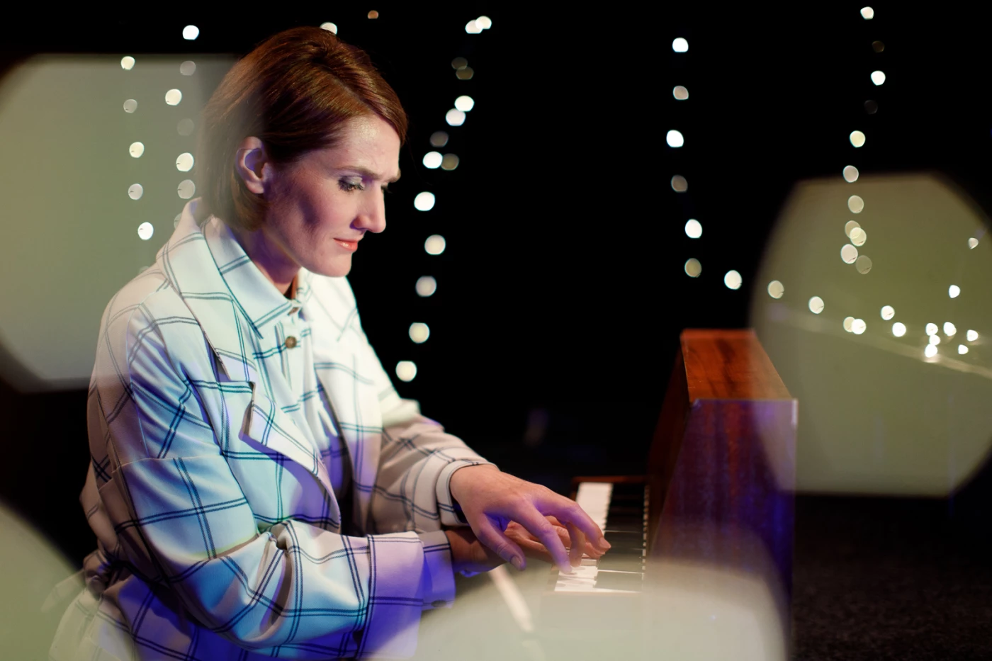 Eine Frau spielt Toy Piano vor einem unscharfen, glitzernden Hintergrund